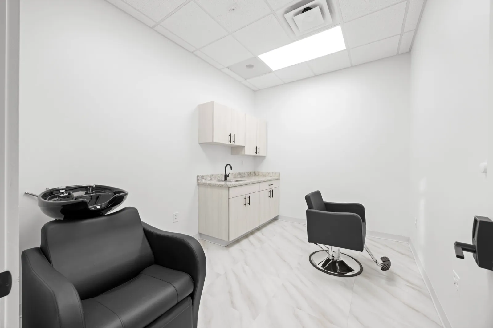 An empty private suite with a shampoo station and styling chair at Revive Salon Collective